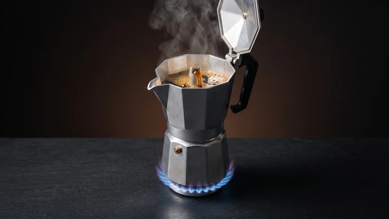 A stovetop aluminium moka pot on a blue gas flame with fresh espresso bubbling and streaming out of the top spout, steam rising.